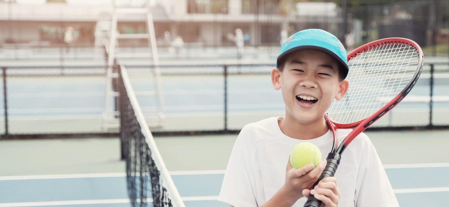 Young tween Asian boy tennis player on outdoor blue court