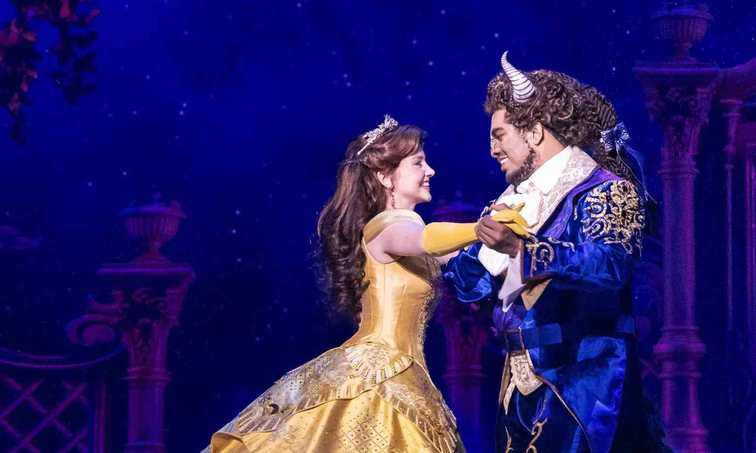 Belle and the Beast dance together on stage under a moonlit sky in Disney’s Beauty and the Beast.